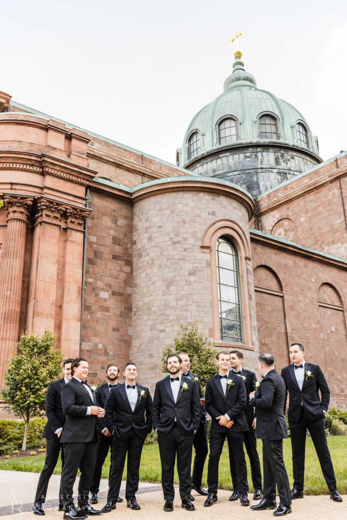 Groom and groomsmen in black tuxes waiting outside of Cathedral Basilica before wedding ceremony in Philadelphia 