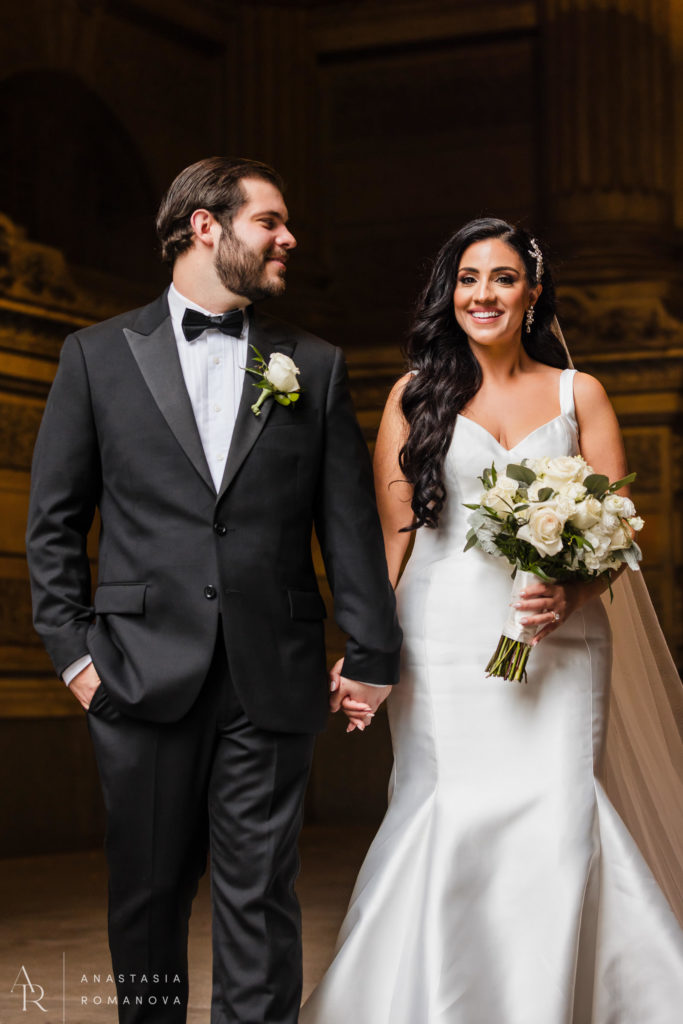 Groom looking lovingly at his bride as they walk holding hands at City Hall in Philadelphia