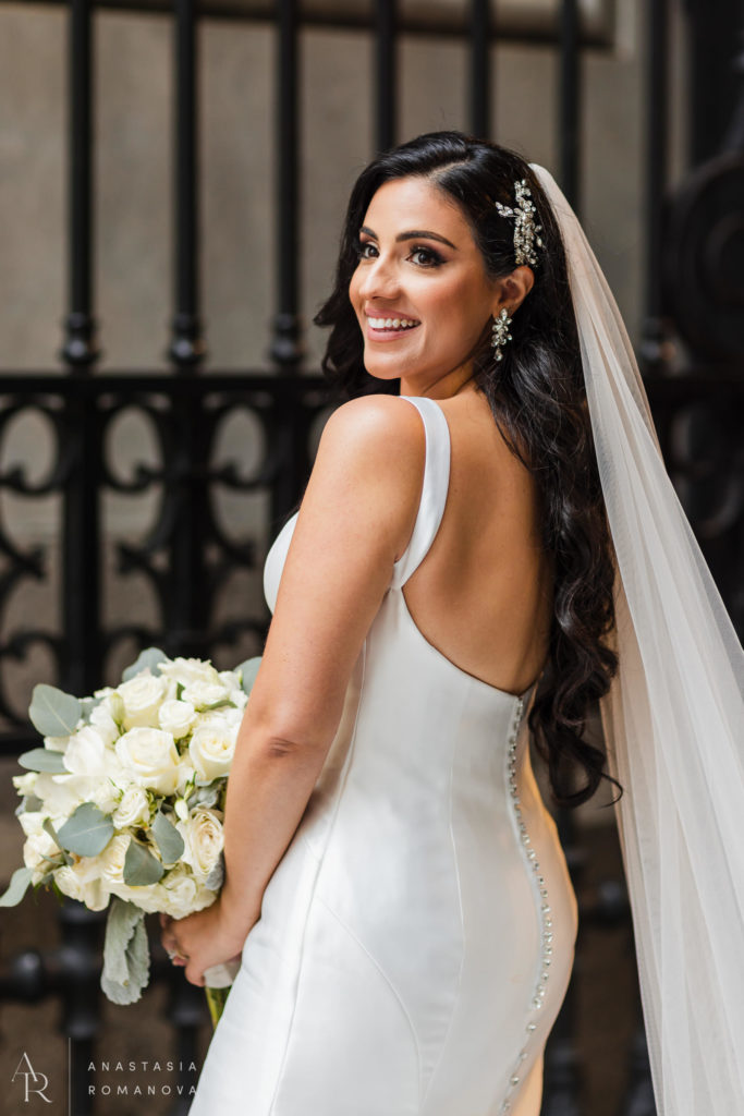 Stunning bride with long black curly hair smiling at teh gates of Philly City Hall